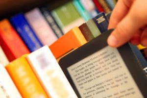 Person taking an e-reader from a book shelf. Selective focus. Very shallow dof. Text in the book is from A Christmas Carol by Charles Dickens (1843).